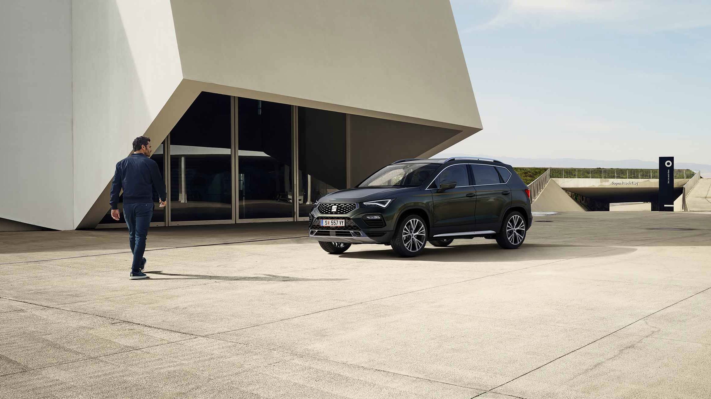 Ein Mann geht auf einen schwarzen SEAT Ateca zu, der vor einem Businessgebäude parkt