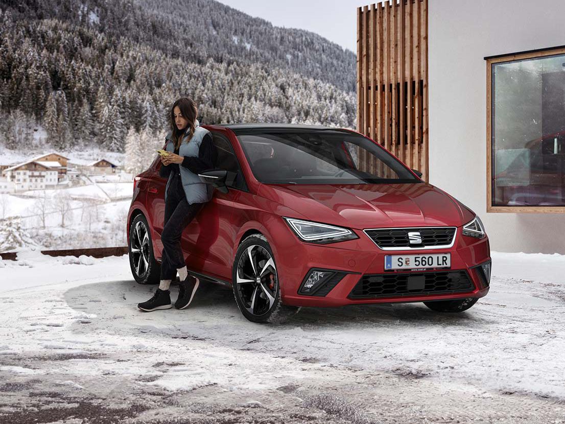 Eine Frau steht neben einem roten SEAT Ibiza in winterlicher Landschaft