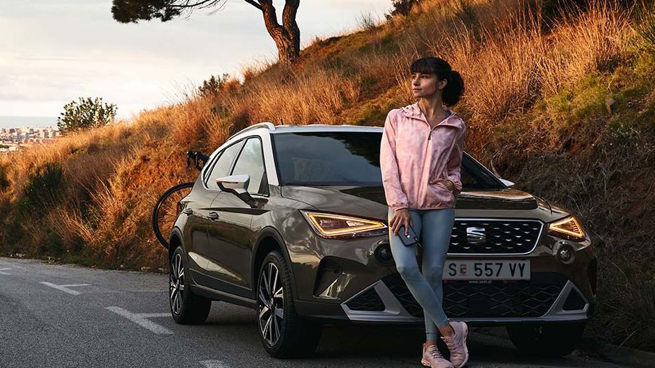Eine Frau lehnt an der Motorhaube eines SEAT Aron