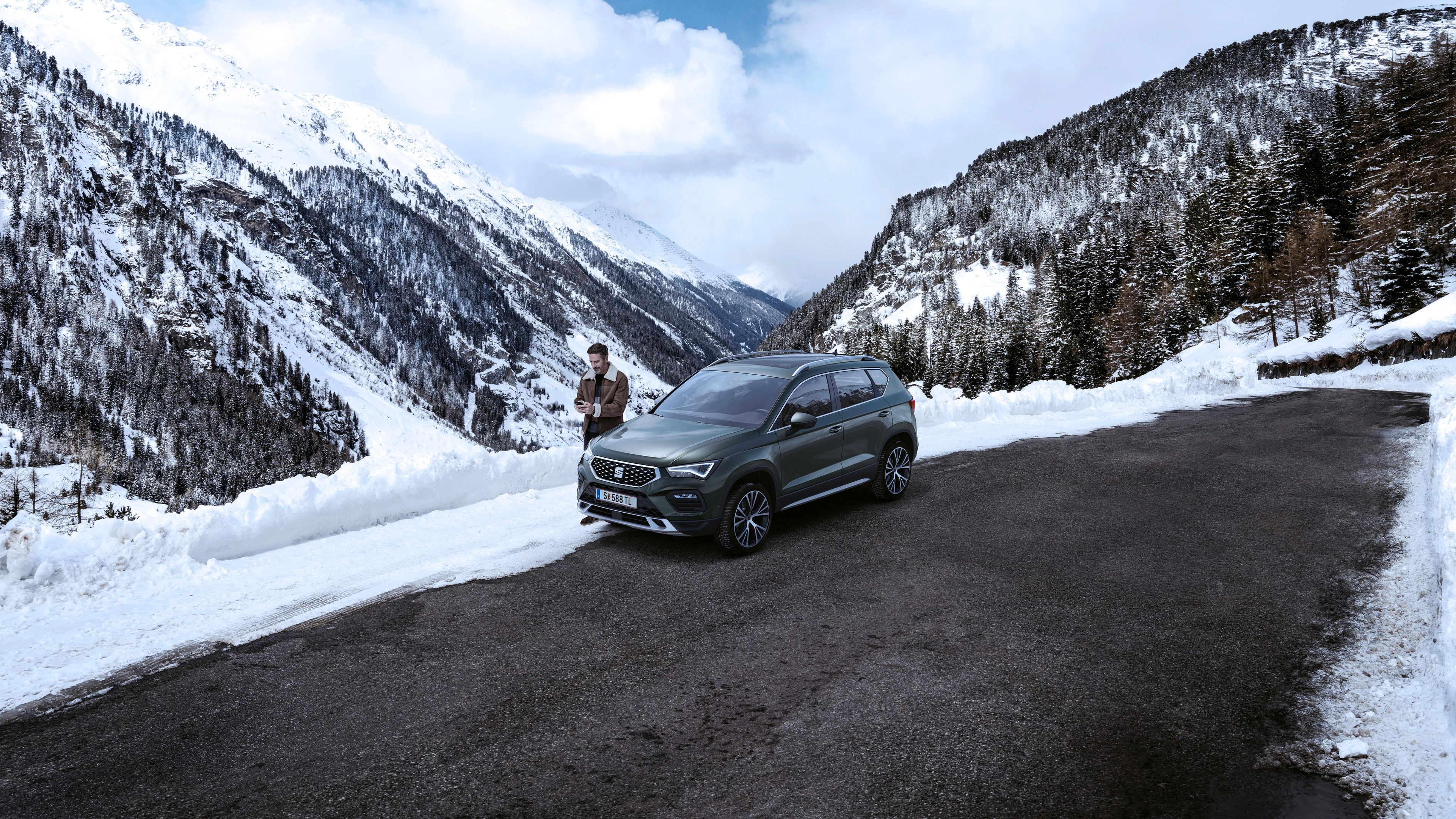 Ein Mann parkt mit seinem dunkelgrünen SEAT Ateca am Straßenrand in einer verschneiten Berglandschaft.
