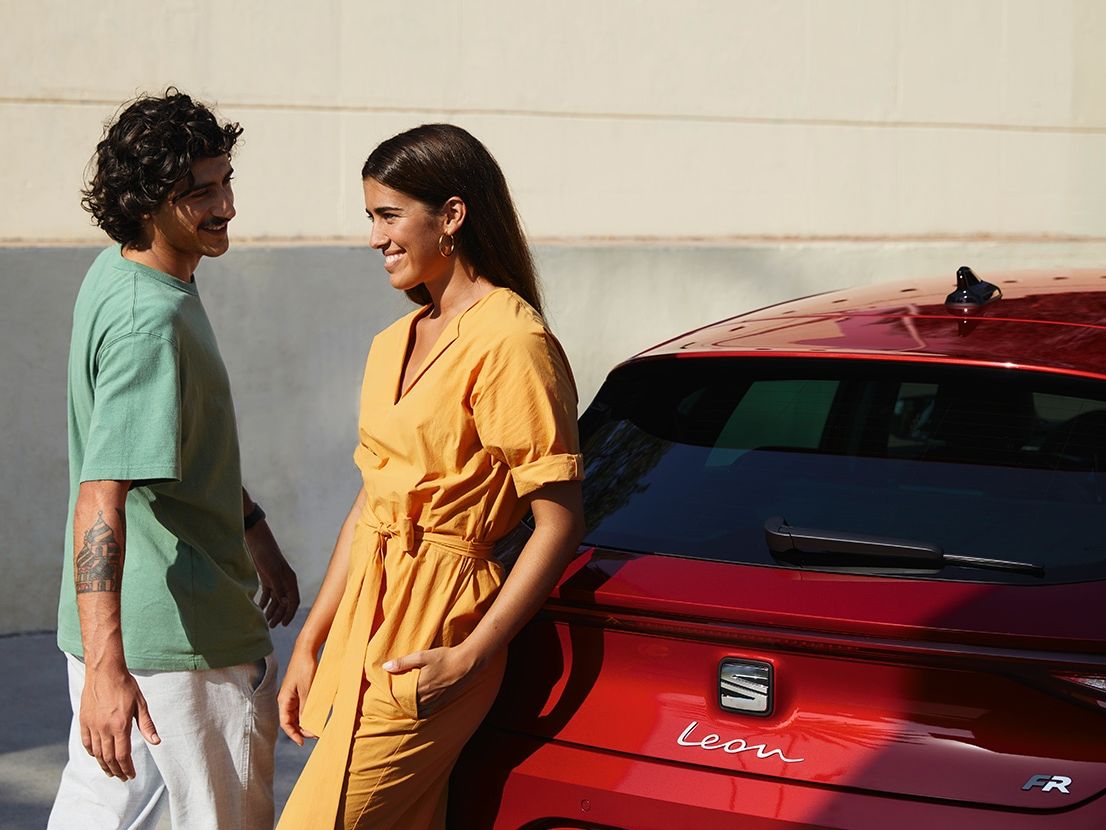 Paar redet miteinander neben einem roten SEAT Leon Sportstourer