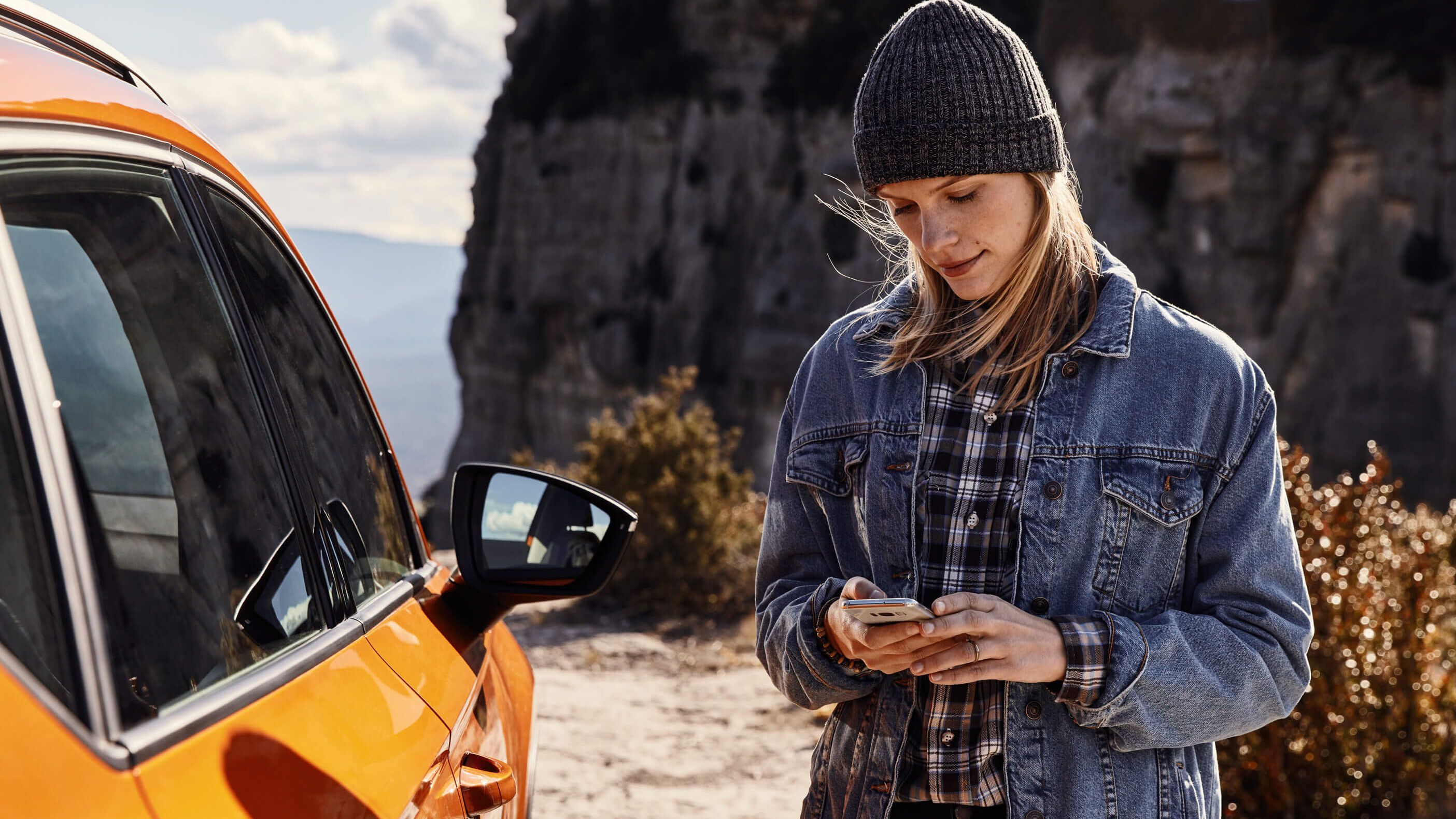 Imagebild zur SEAT % Jahres Garantie mit einer Frau die vor einem orangen SEAT auf ihr Smartphone blickt