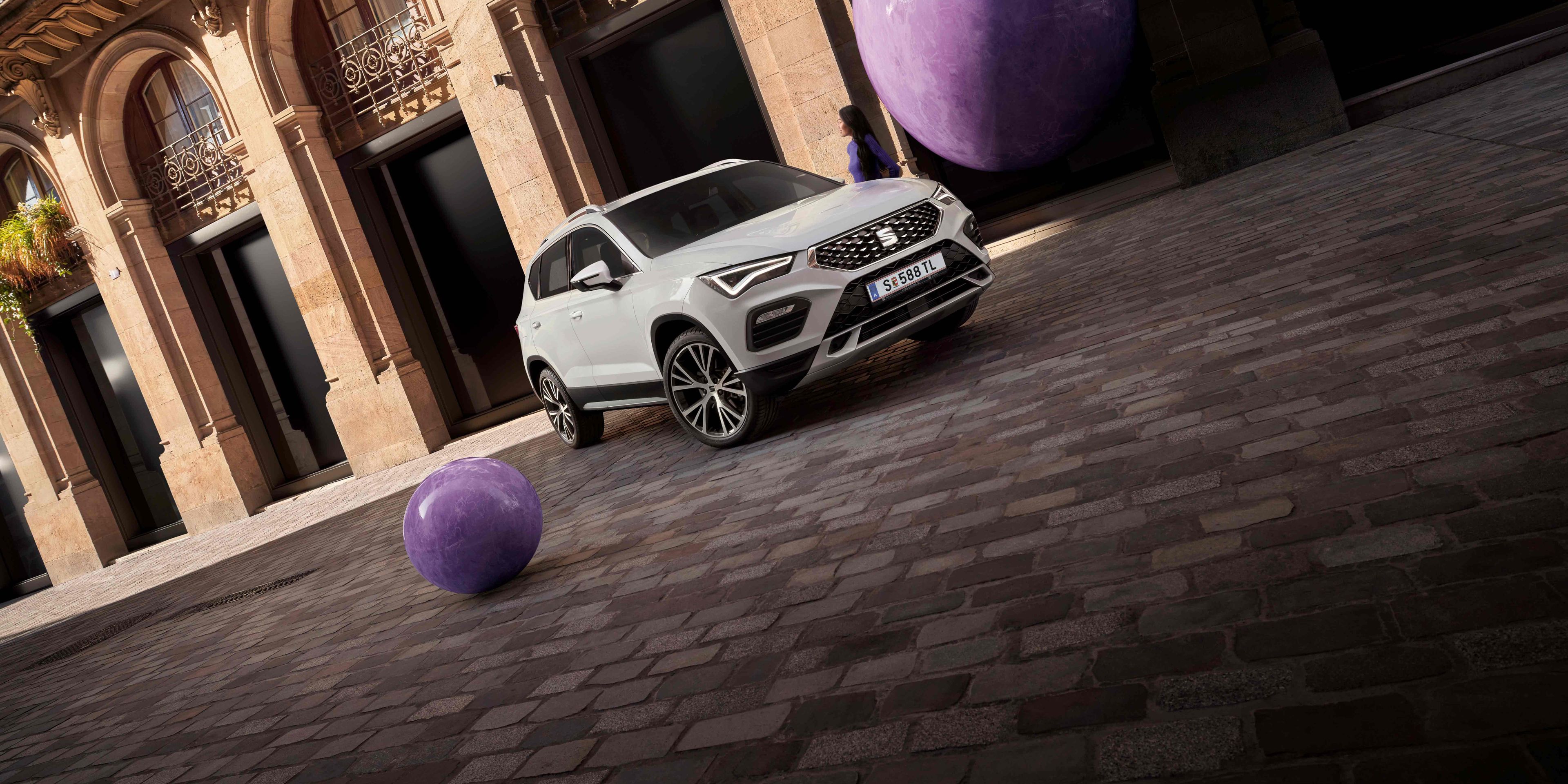 Ein weißer SEAT Ateca  steht perspektivisch aufgenommen vor einem älteren aber eleganten Gebäude