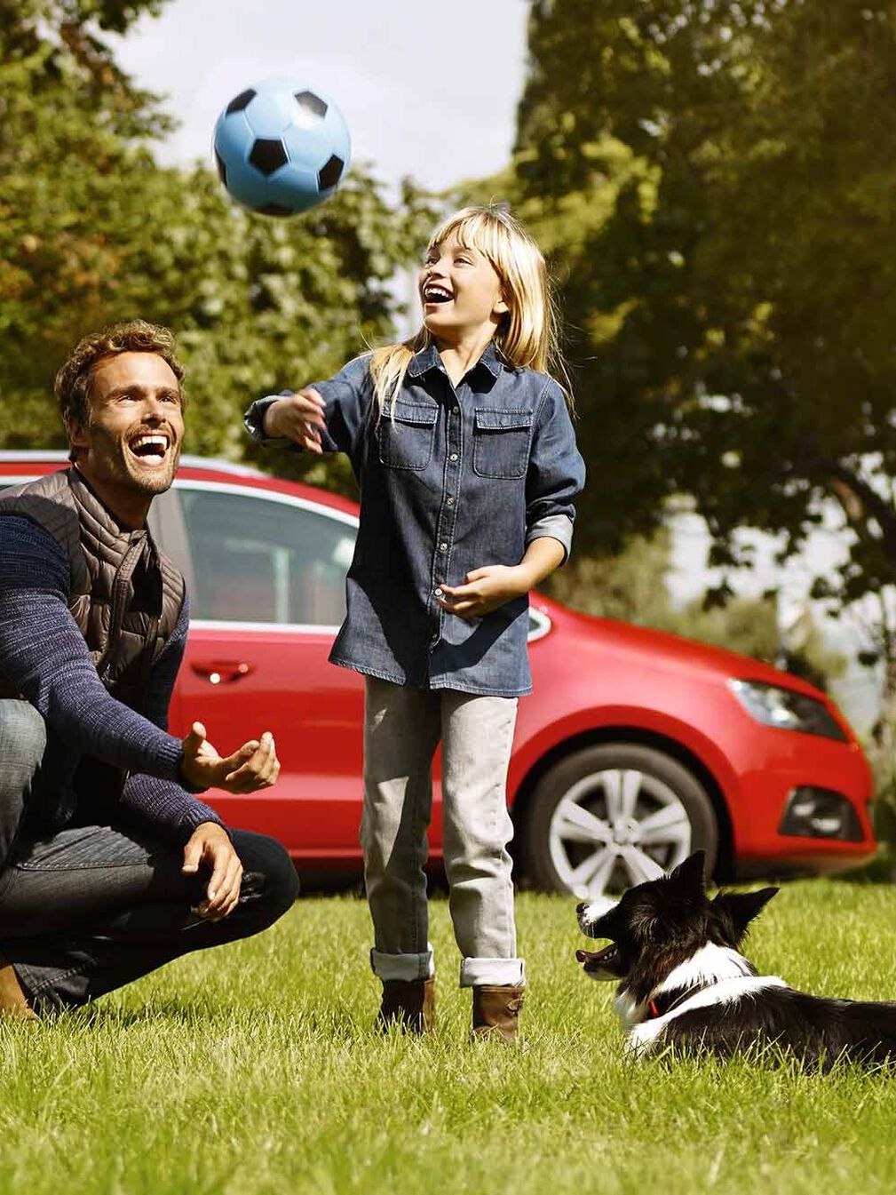 Im Hintergrund parkt ein roter SEAT Alhambra, während ein Vater gemeinsam mit seiner Tochter und ihrem Hund auf einer Wiese Ball spielt