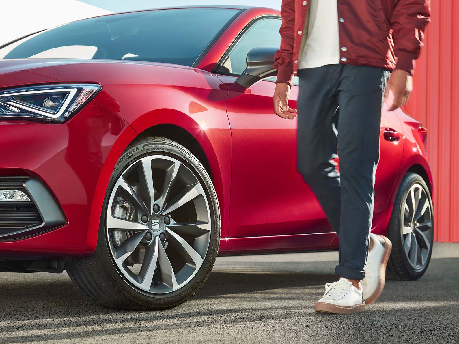 Ein Mann steht neben einem SEAT Leon Desire in Rot mit Cosmo-Grauem Leichtmetallrad