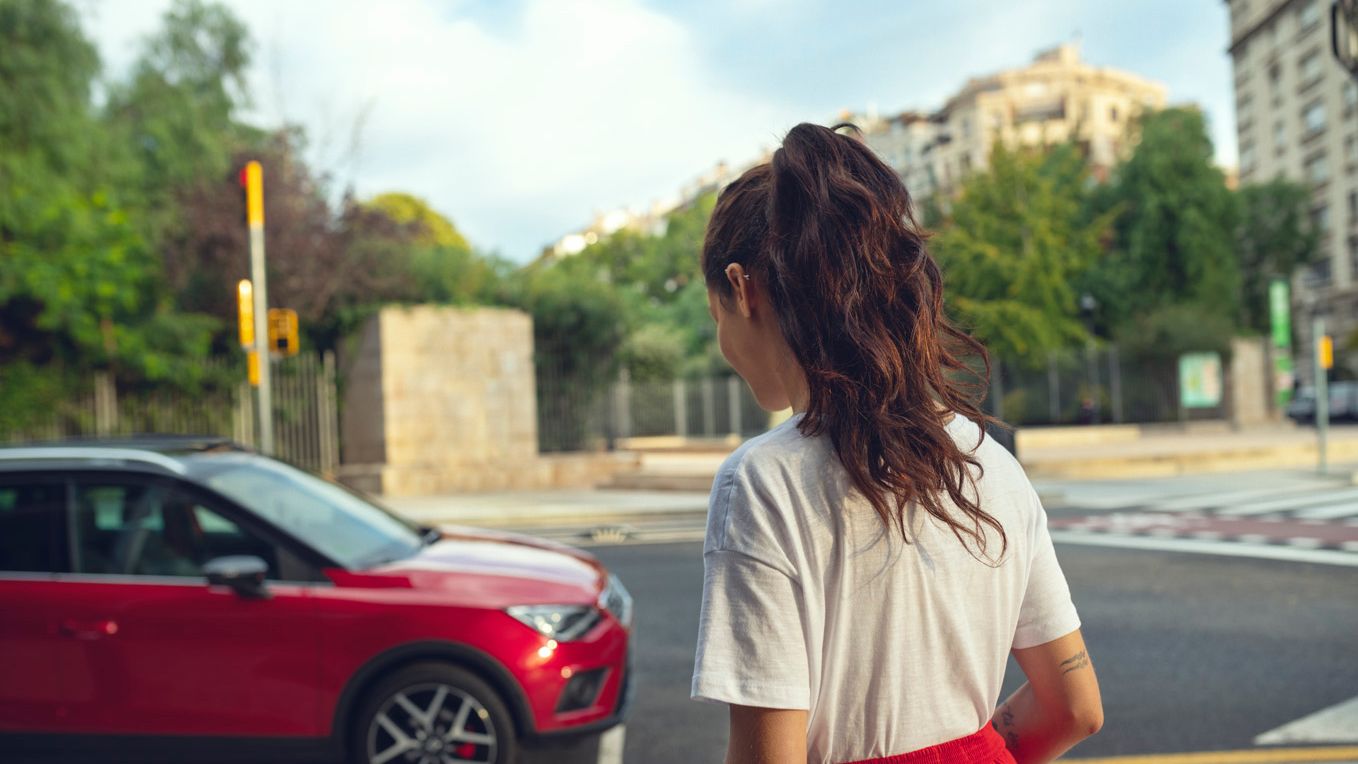 Eine Frau nähert sich einem roten SEAT Arona, der an der Straßenseite steht