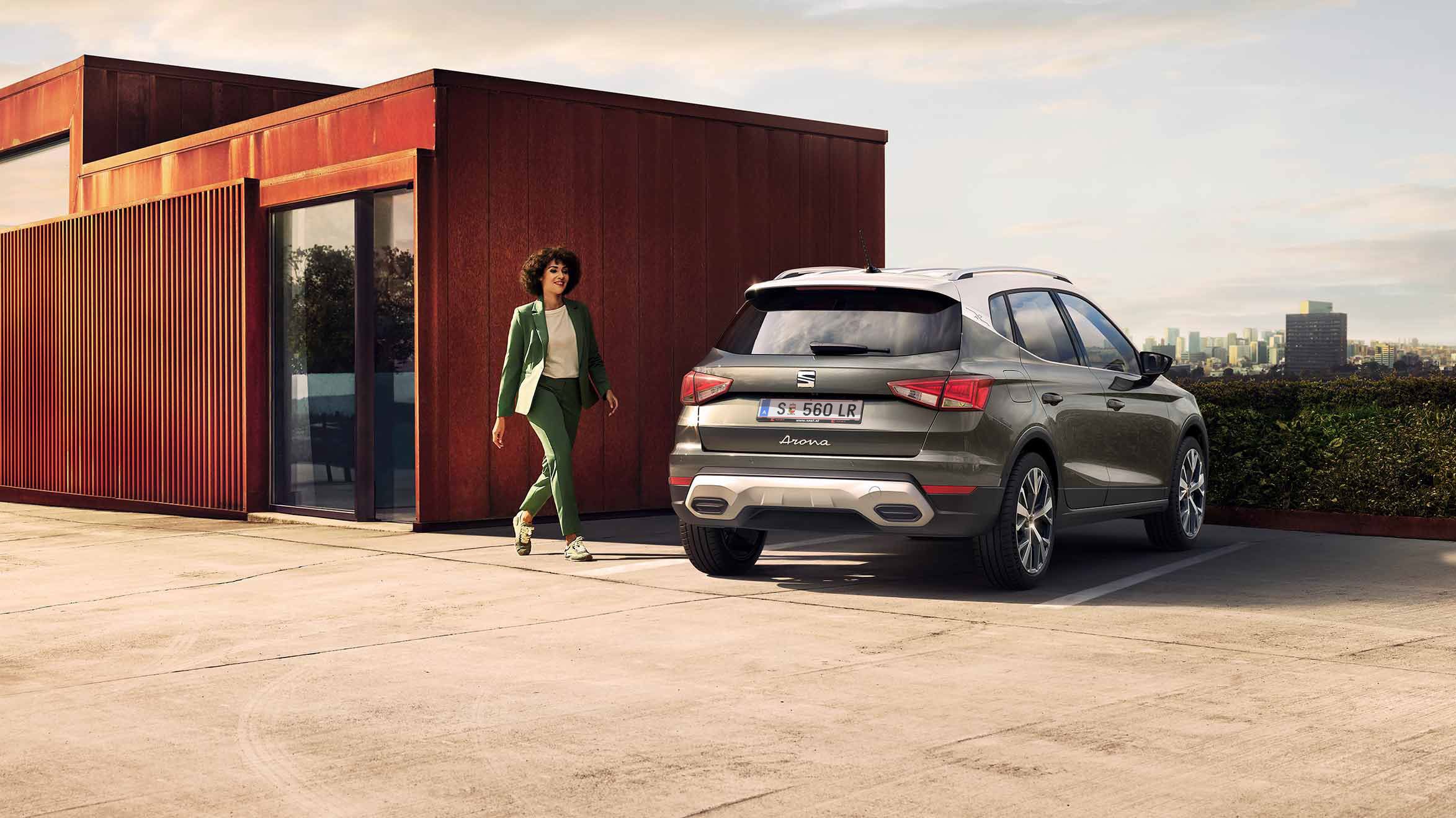 Eine Frau geht zu ihrem SEAT Arona in Cliff Grey auf einem Parkplatz