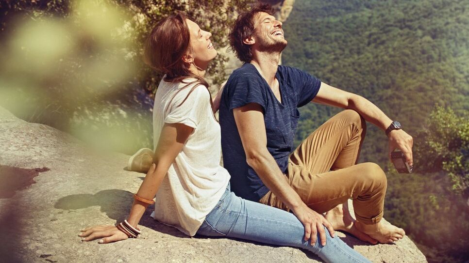 Eine Frau und ein Mann sitzen auf einem Felsen in der Natur.