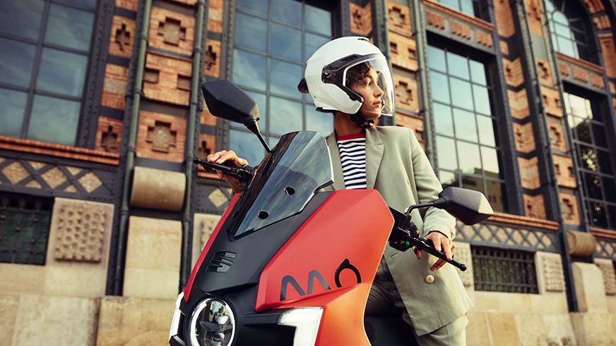 Eine Frau sitzt auf einen roten SEAT MO 125 Electric Scooter 