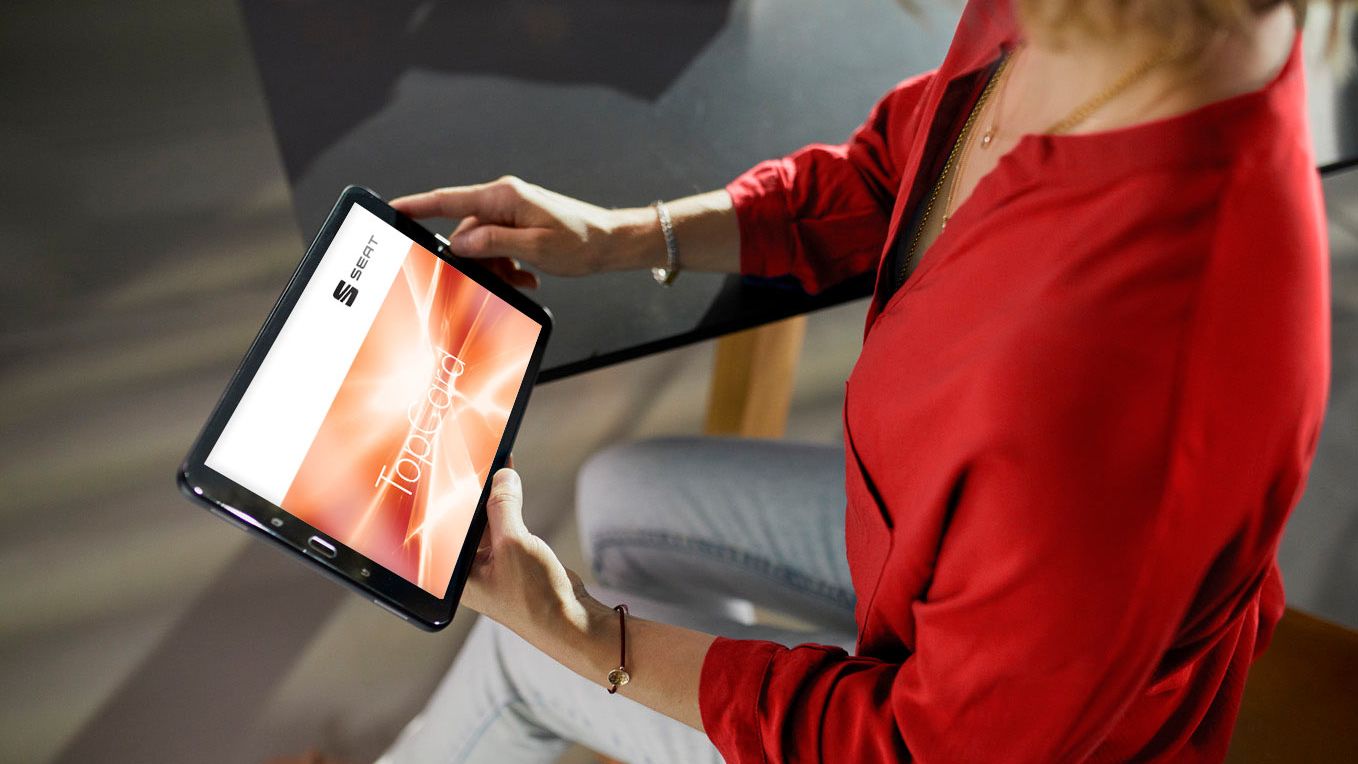 Eine Frau hält ein Tablet in der Hand und präsentiert die SEAT TopCard