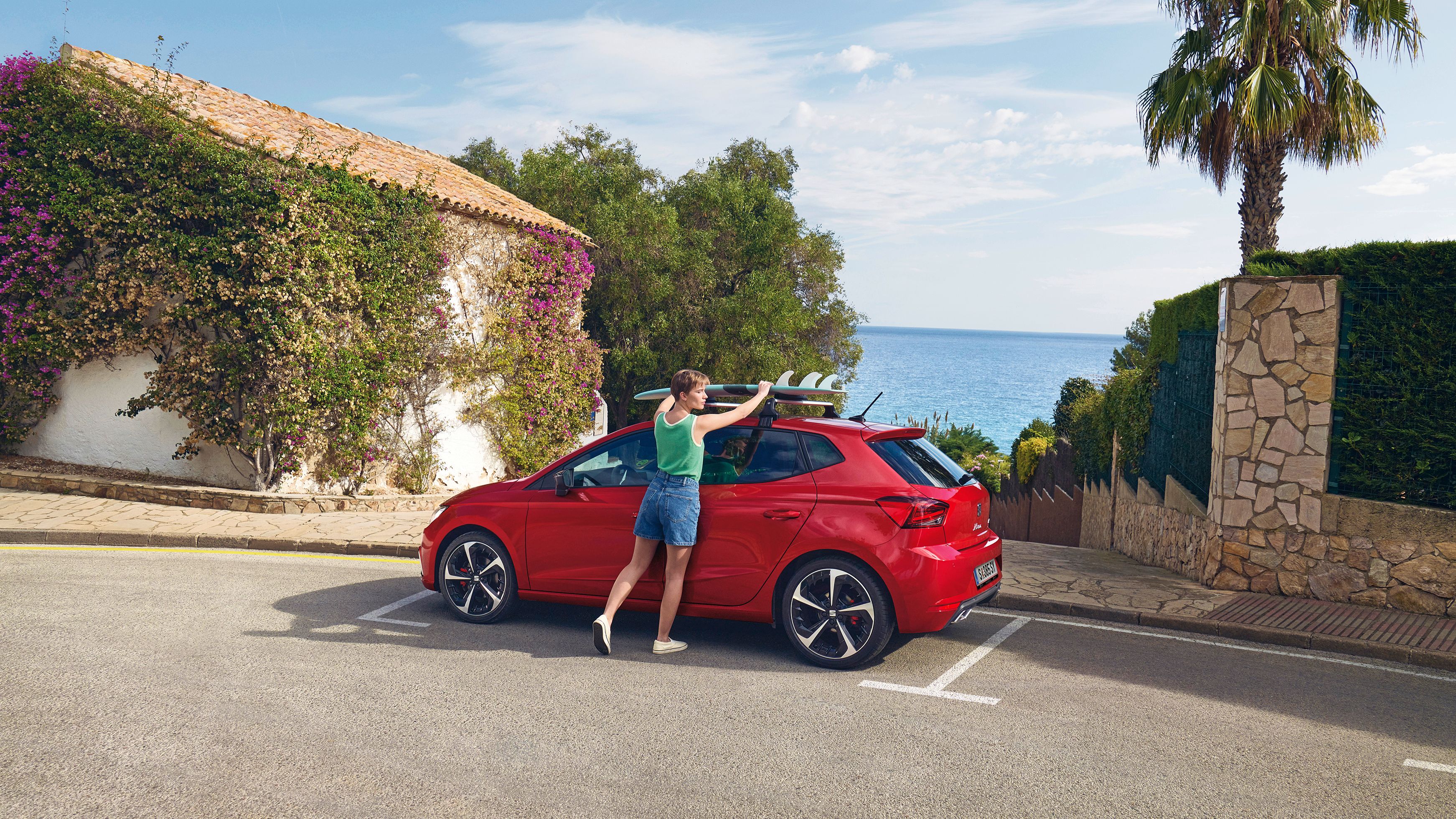 Eine Frau befestigt ein Surfbrett auf dem Dachträger eines roten SEAT Ibiza