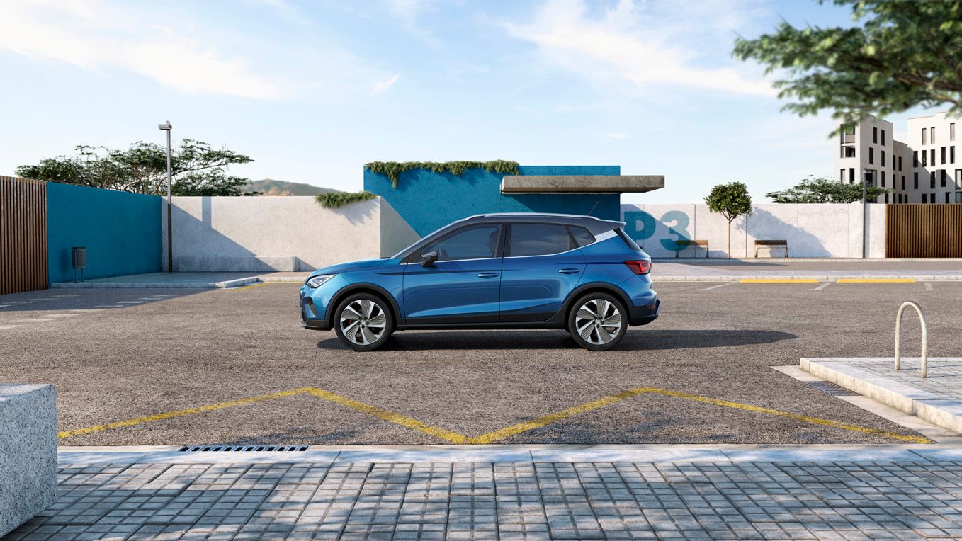 Ein blauer SEAT Arona ist in Seitenansicht zentral auf einem Parkplatz positioniert