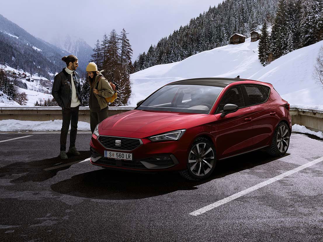 Paar redet miteinander neben einem roten SEAT Leon in Schneegebirge