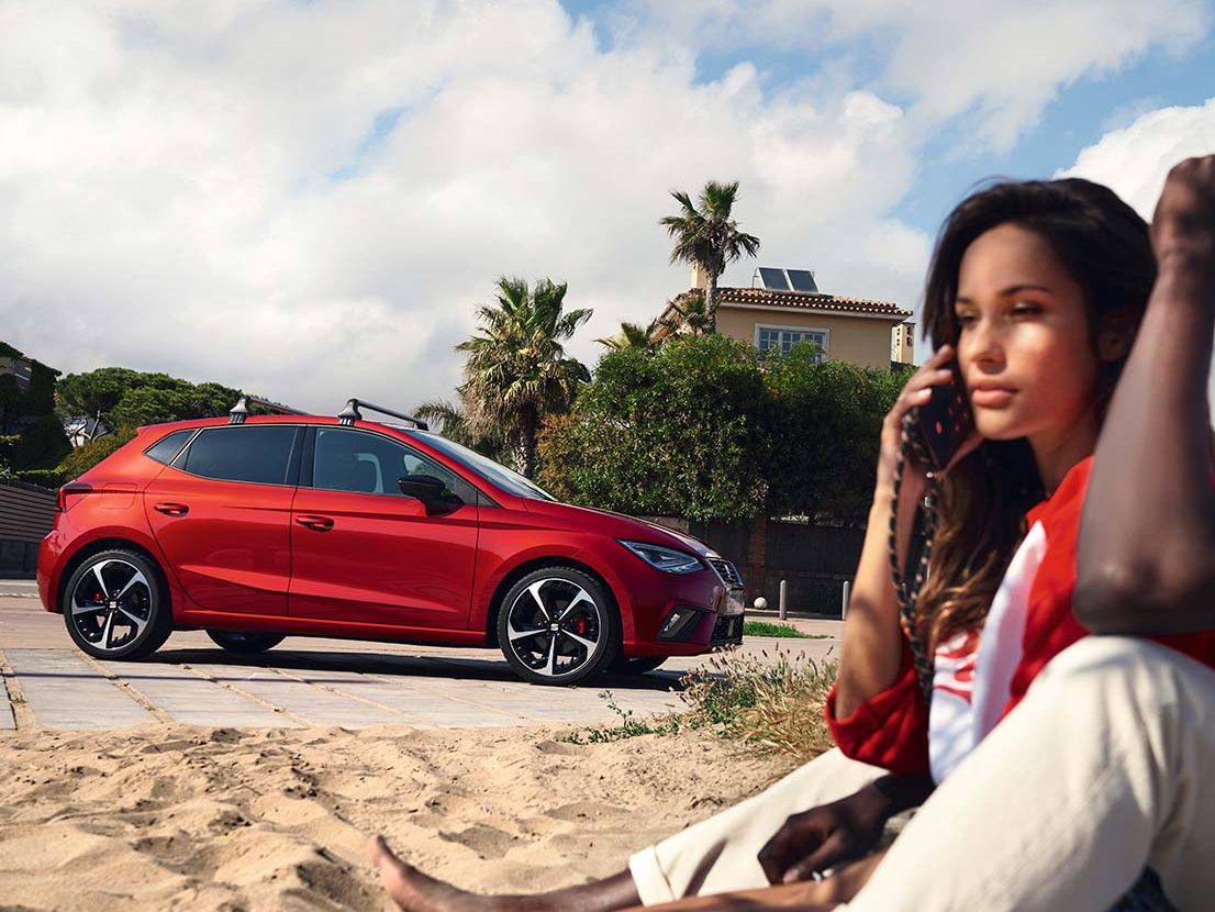 Eine Frau telefoniert, im Hintergrund befindet sich eine roter SEAT Ibiza.