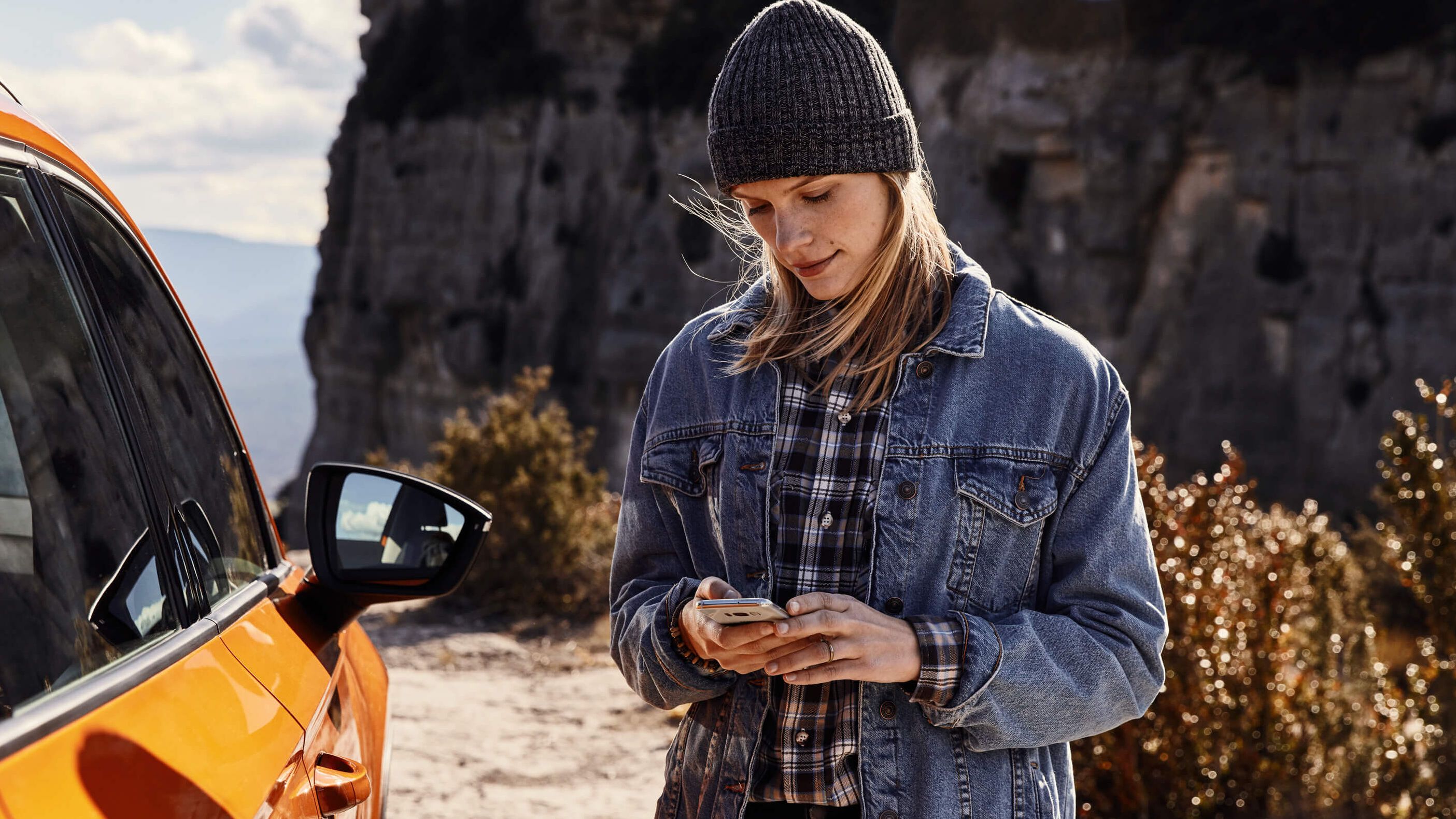 Eine Frau hält ihr Smartphone in der Hand und steht vor einer Klippe 