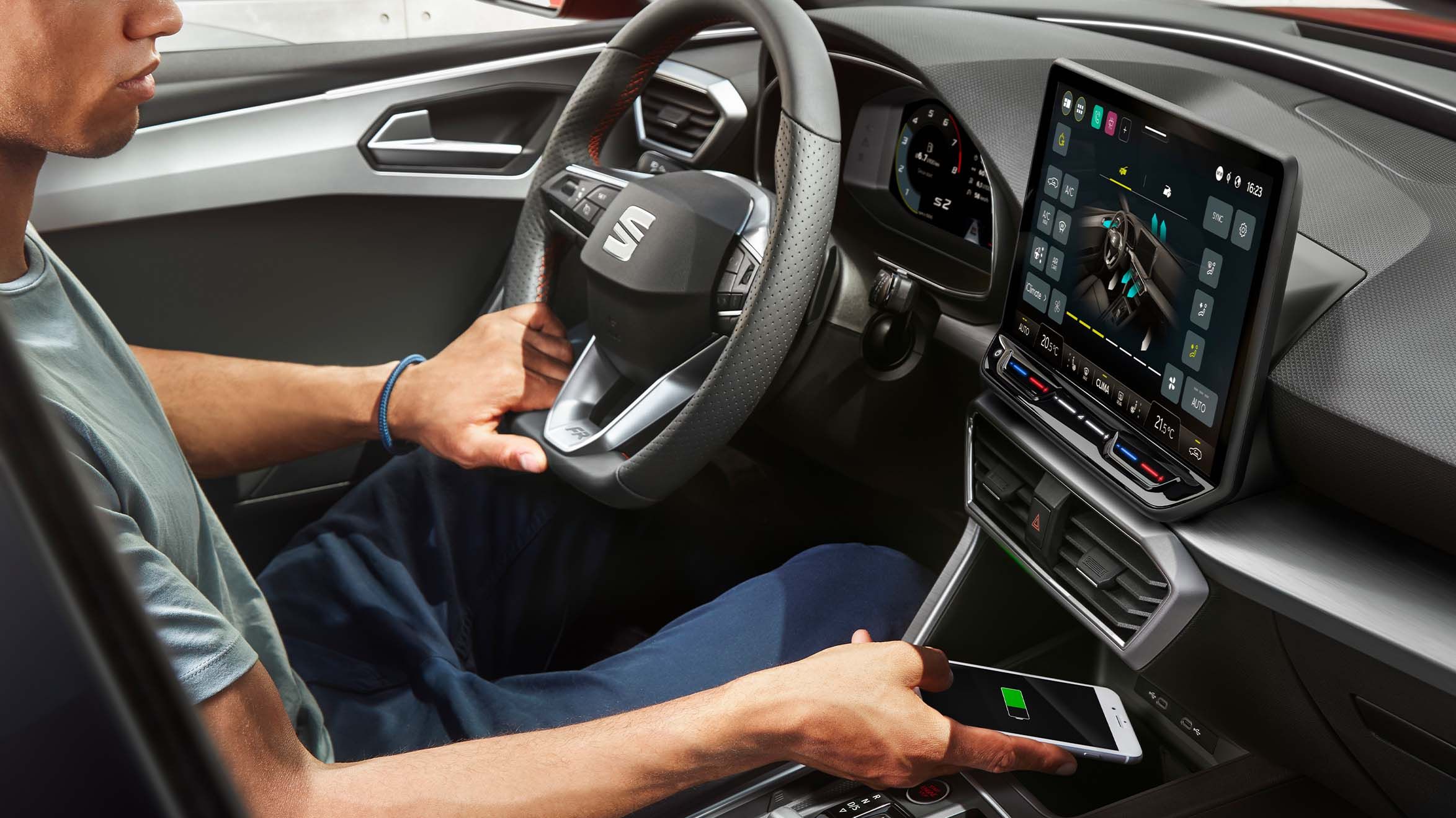 Ein Fahrer befinden sich im Fahrzeug - SEAT Connect Digital Cockpit und das zentrale Display zeigen relevante Informationen an. Ein Smartphone wird gerade in die induktive Ladestation gelegt