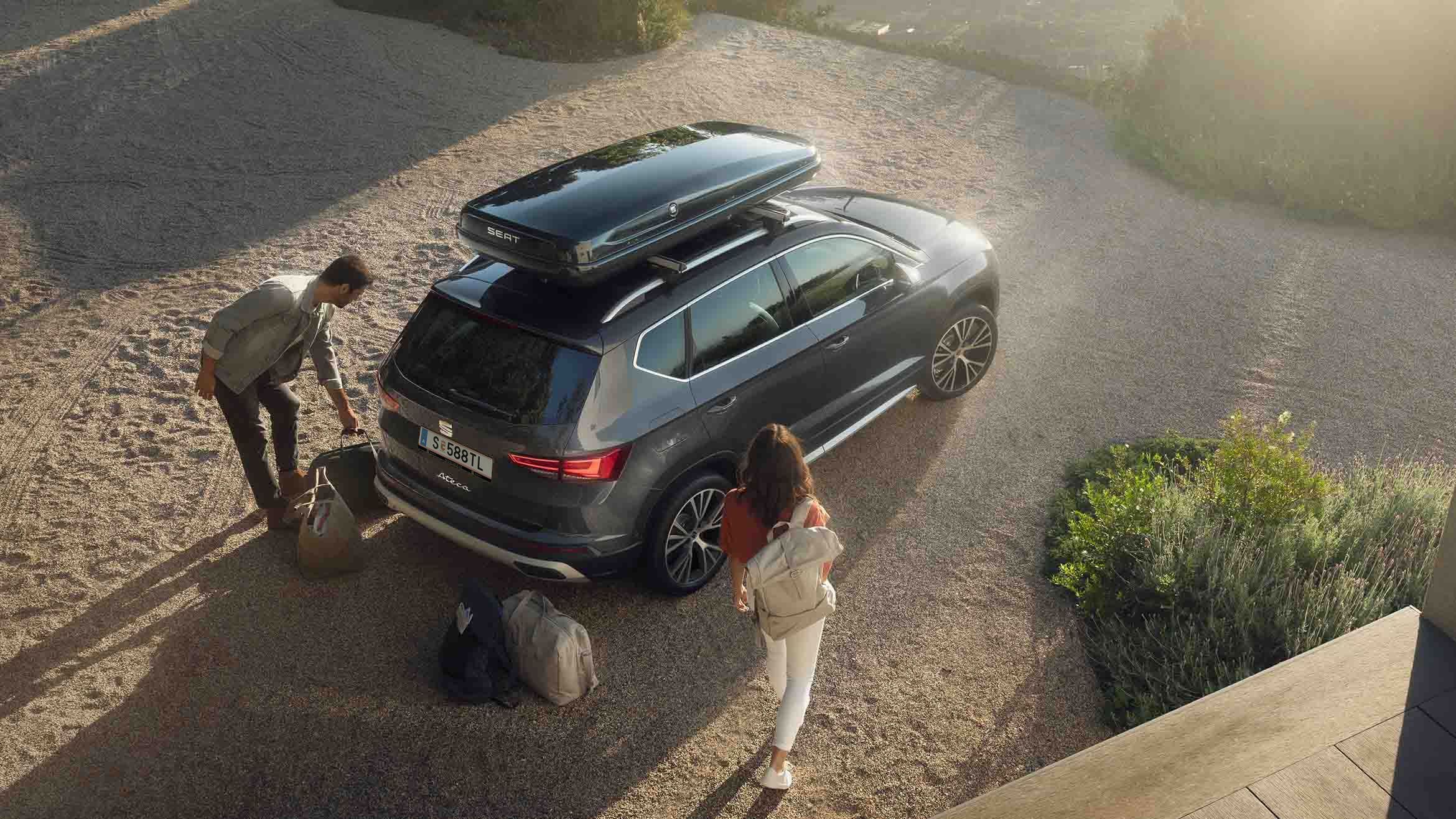 Ein graphitegrauer SEAT Ateca mit Dachbox – ein Paar packt ein und macht sich bereit für den nächsten Trip