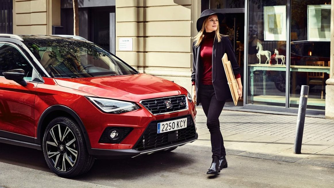 Eine Frau läuft mit einem Paket in der Hand an einem roten, geparkten SEAT vorbei