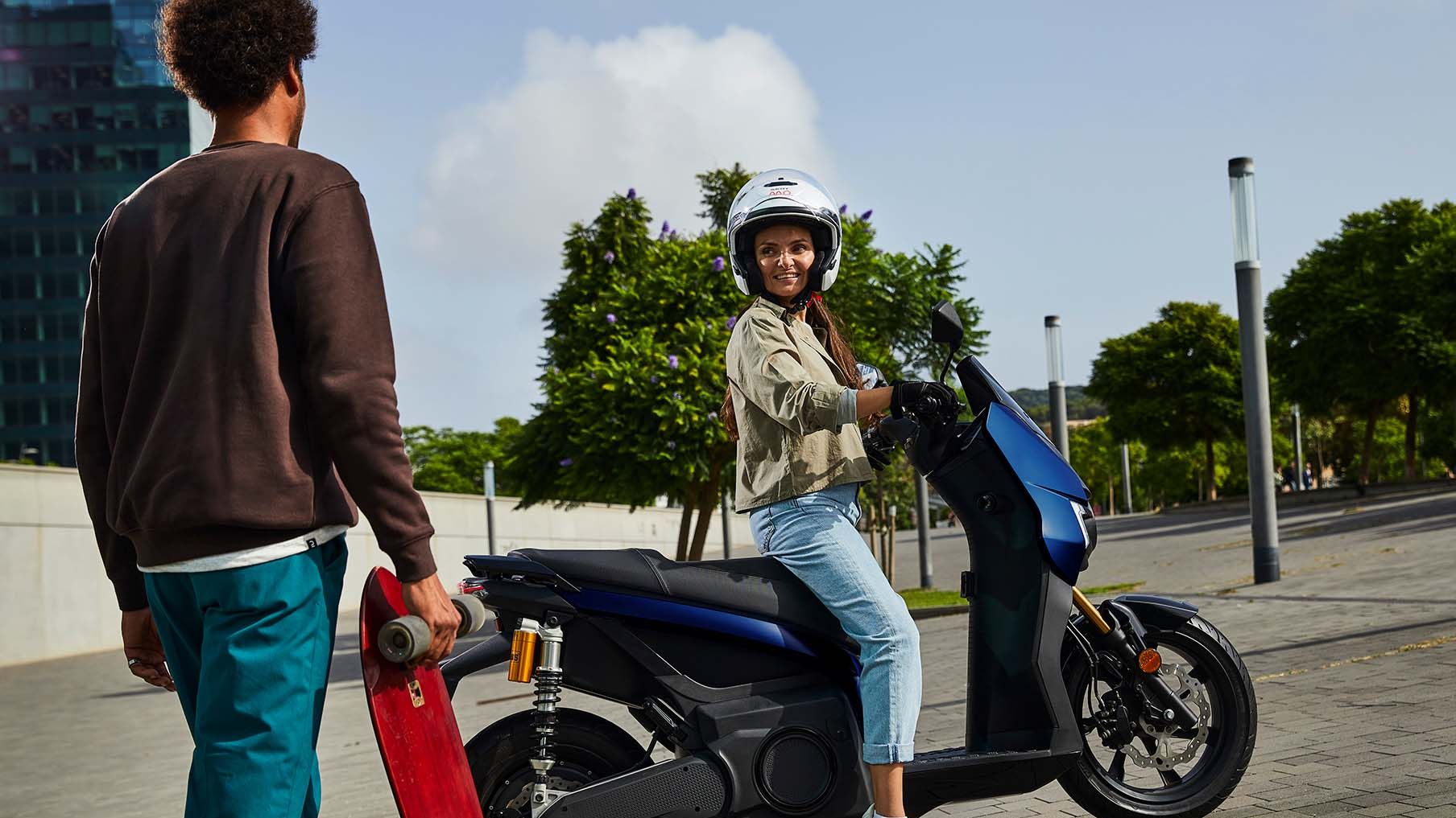 Eine Frau auf einem SEAT MÓ 125 Performance unterhält sich mit einem Skateboarder