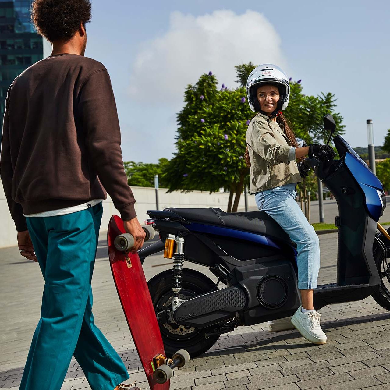 Eine Frau auf einem SEAT MÓ 125 Performance unterhält sich mit einem Skateboarder