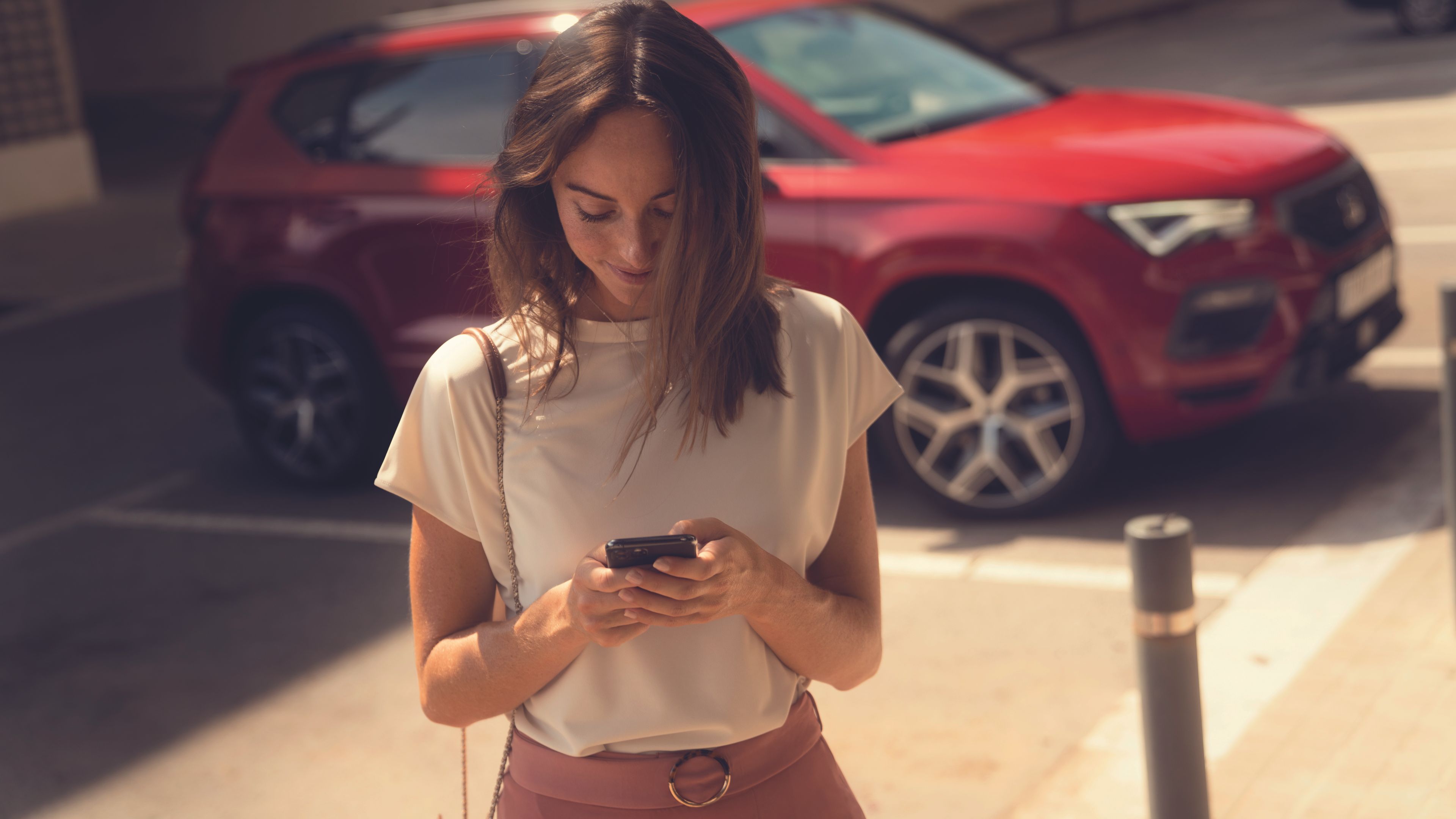 Eine Frau blickt auf ihr Smartphone, im Hintergrund ist ein roter SEAT Ateca zu sehen