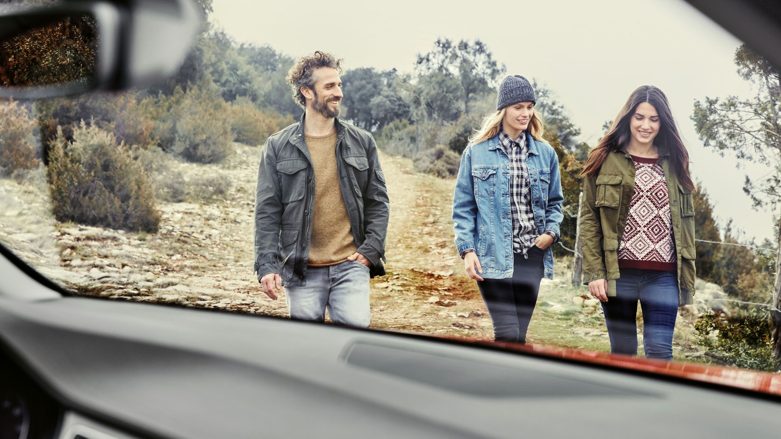 Drei Personen gehen gerade von einem Waldstück Richtung Auto zurück 