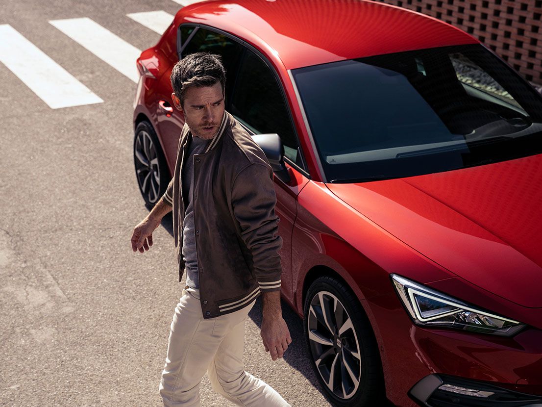 Ein Mann geht von einem SEAT Leon in Desire Red mit Leichtmetallfelgen weg