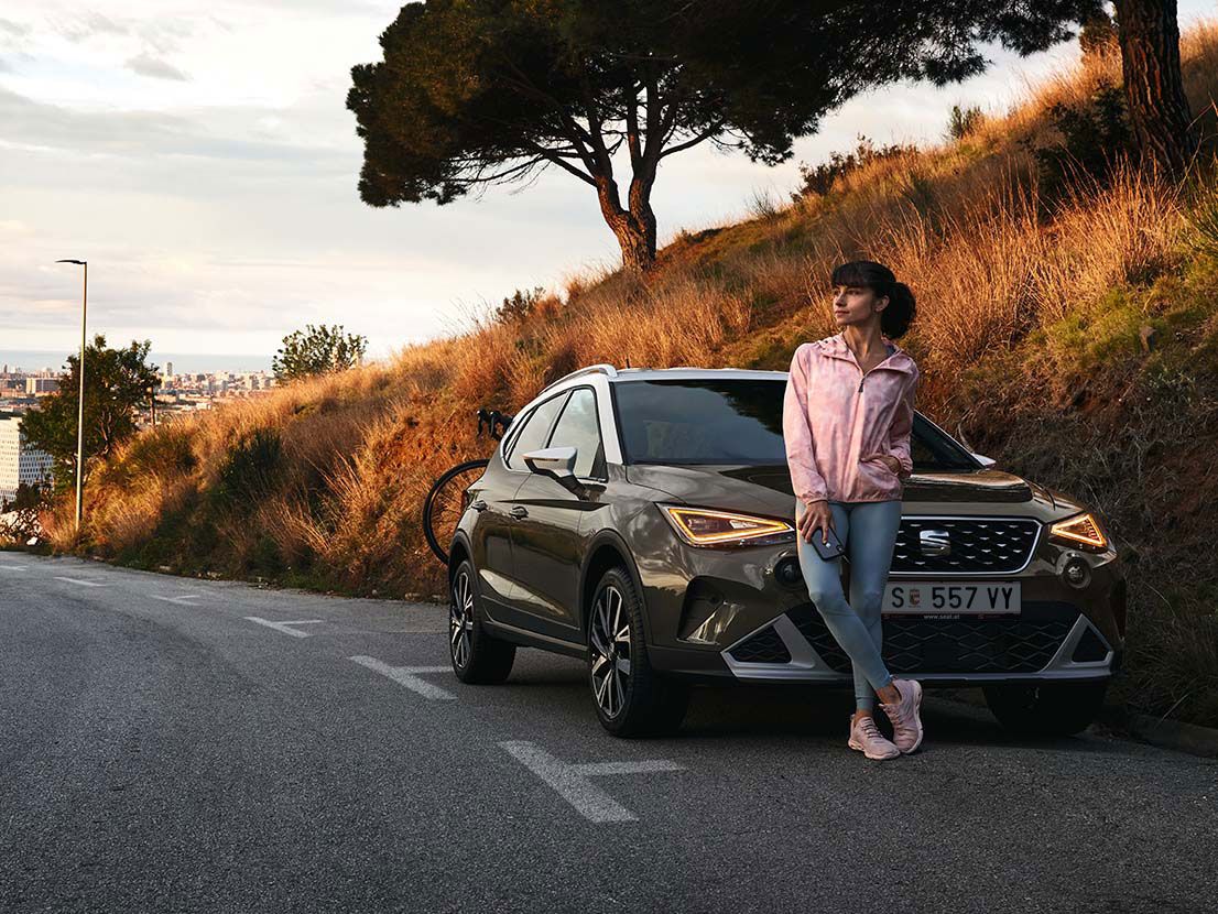 Eine Frau lehnt an der Motorhaube eines SEAT Aron