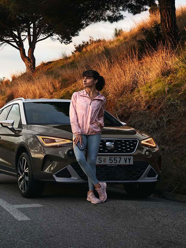 Eine Frau lehnt an der Motorhaube eines SEAT Aron