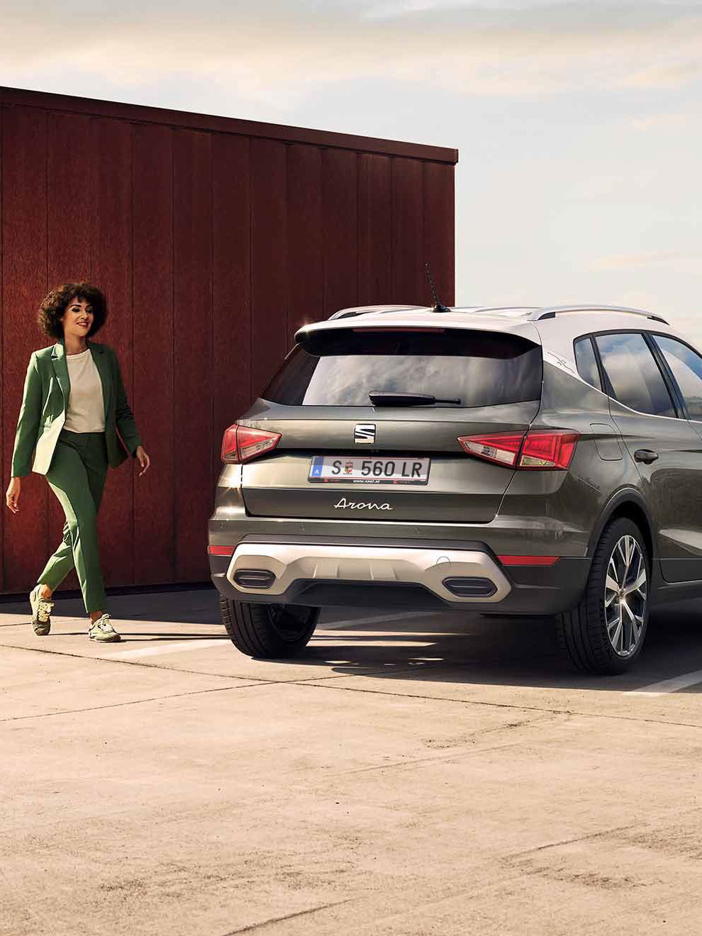 Eine Frau geht zu ihrem SEAT Arona in Cliff Grey auf einem Parkplatz