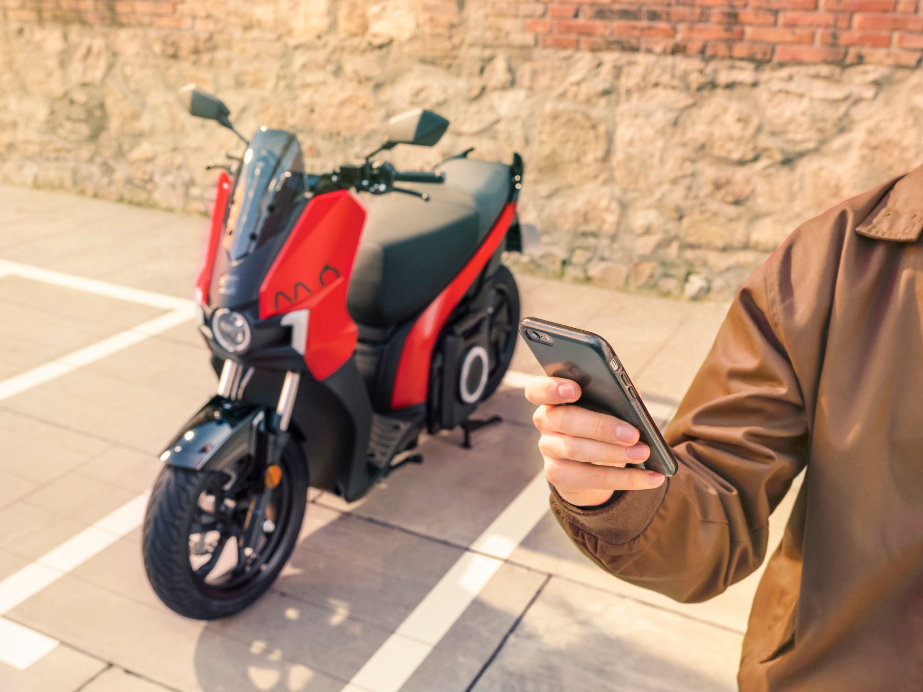 Eine Person hält ein Smartphone in der Hand, im Hintergrund steht ein SEAT MO 125.