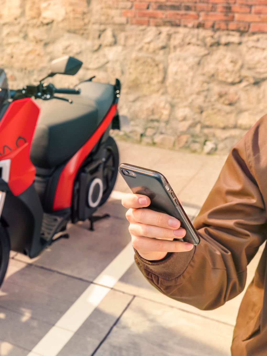 Eine Person hält ein Smartphone in der Hand, im Hintergrund steht ein SEAT MO 125.