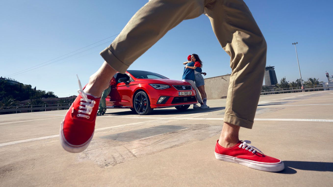 Eine Freundgruppe steht um einen roten SEAT Ibiza 
