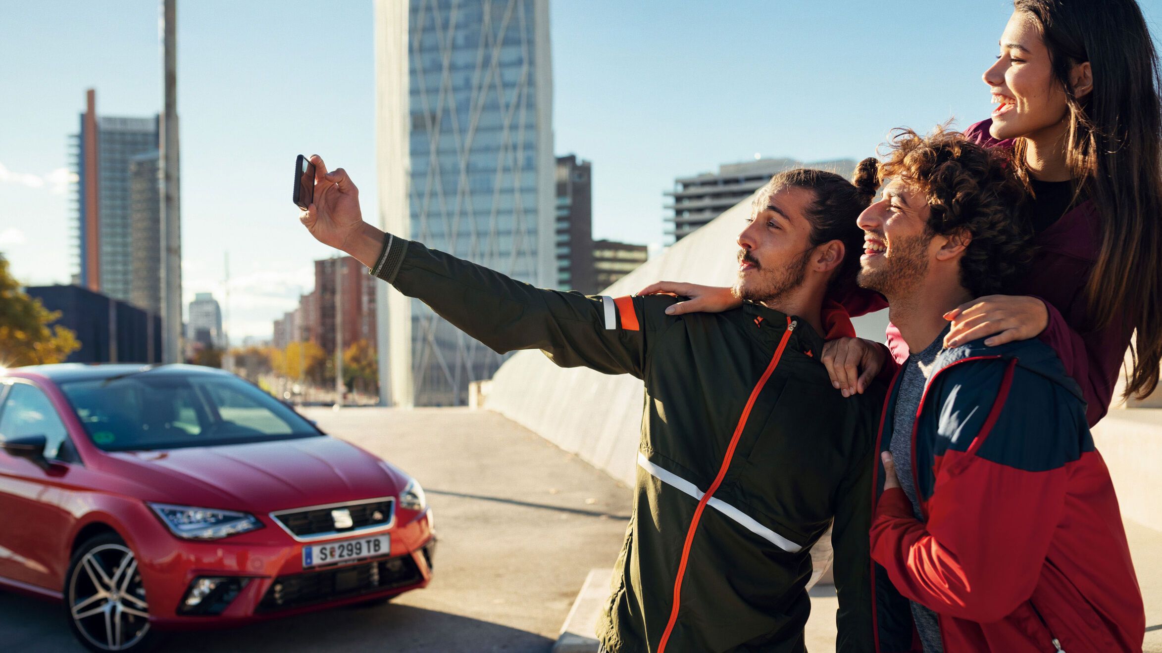 Drei Personen machen gerade ein Selfie. Im Hintergrund ist ein roter SEAT zu sehen.