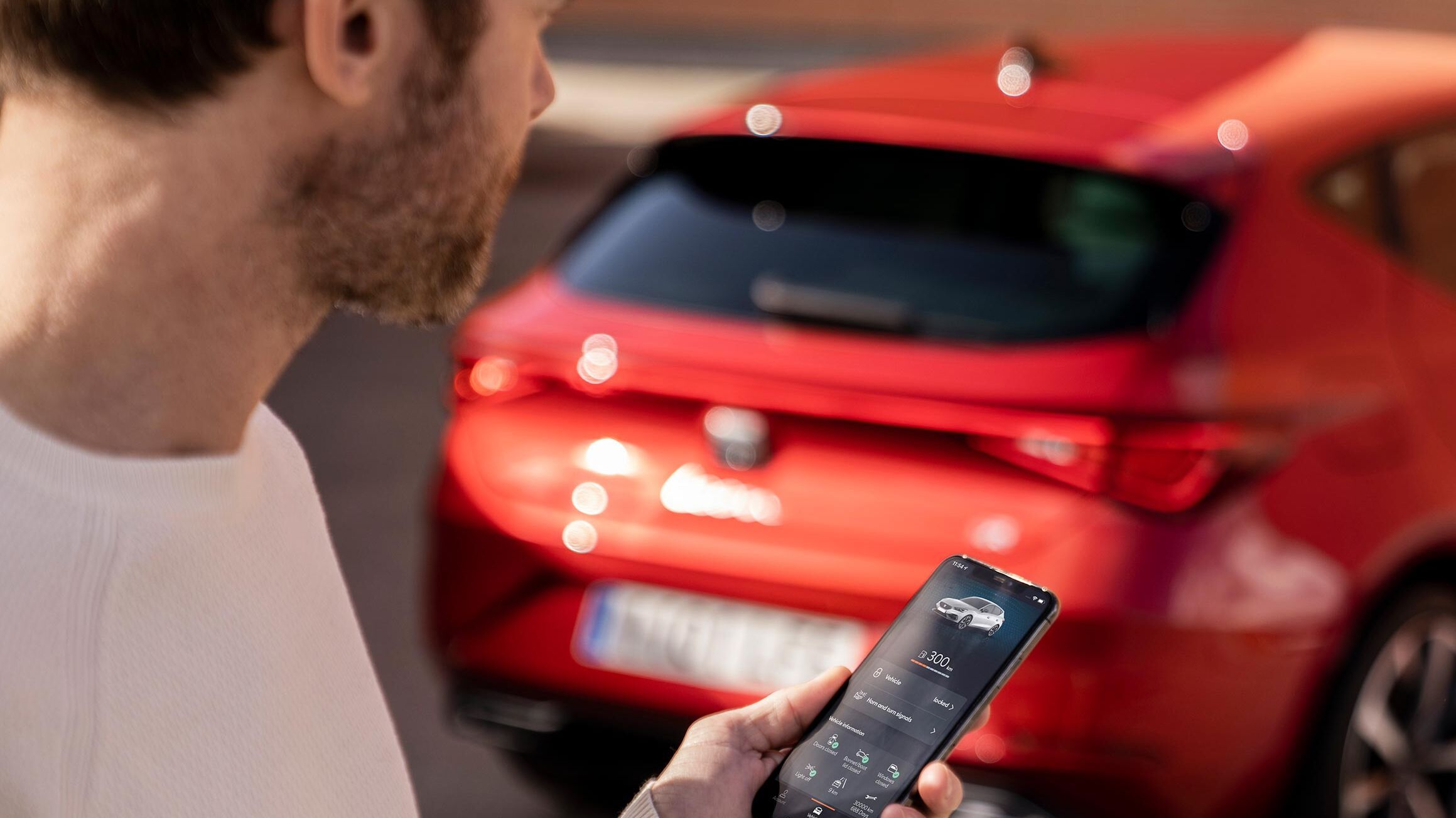 Ein Mann mit einem Smartphone in der Hand steht vor einem roten SEAT.