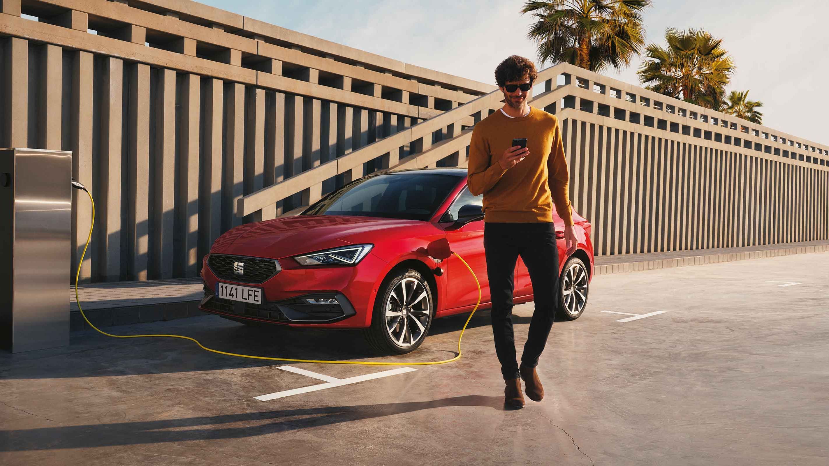 Ein Mann lädt seinen SEAT Leon Hybrid, checkt dabei die SEAT Connect App und geht dann vom Auto weg