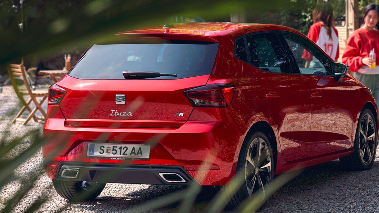 Roter SEAT Ibiza steht auf einen Schotterplatz und im Hintergrund sind Frauen mit einem Getränk in der Hand 