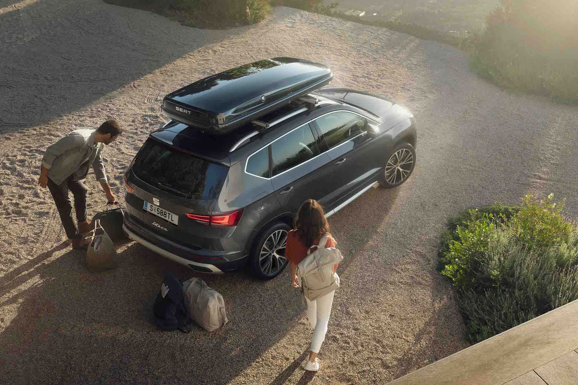 Ein graphitegrauer SEAT Ateca mit Dachbox – ein Paar packt ein und macht sich bereit für den nächsten Trip