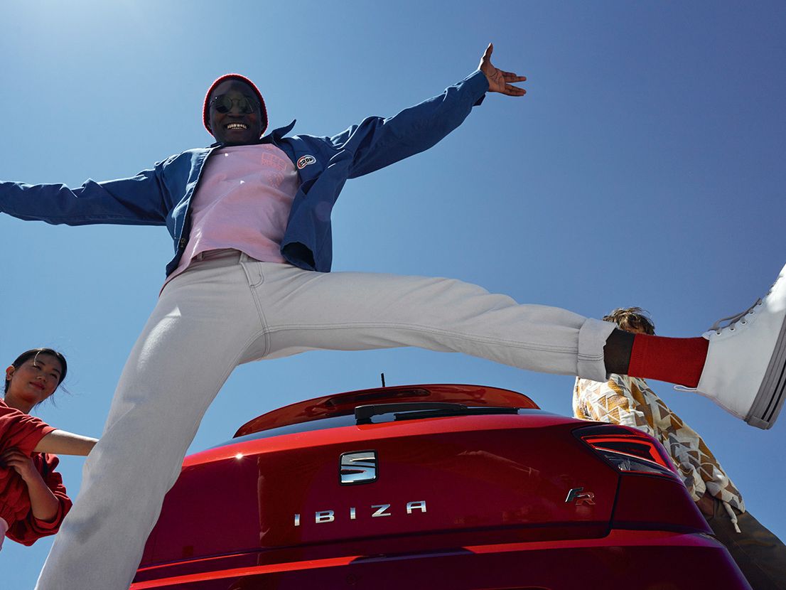 Ein Mann springt hinter einem roten SEAT Ibiza hoch