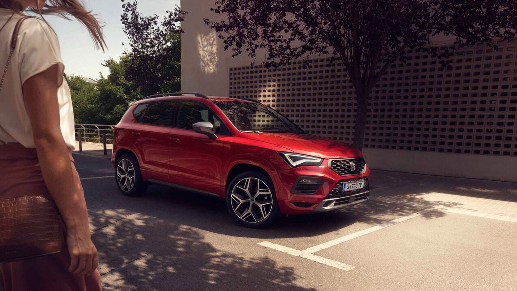 Ein roter SEAT Ateca ist am Straßenrand geparkt, während eine Frau auf das Fahrzeug zugeht