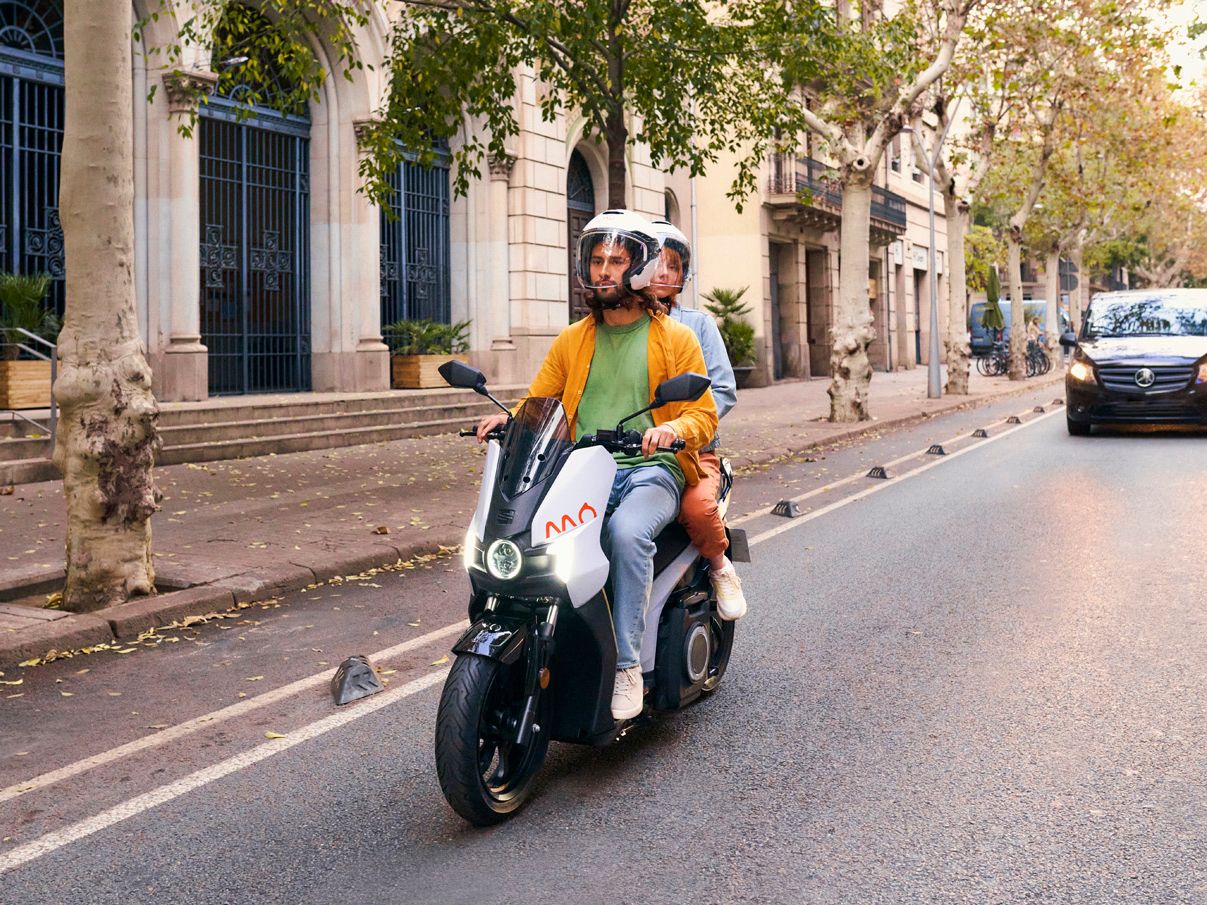 Ein Mann und eine Frau fahren mit einem SEAT MO 125 in der Farbe Oxygen White Matt.