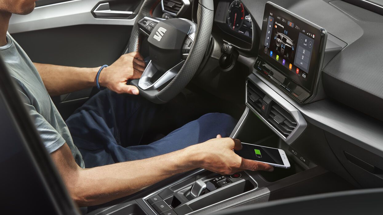 Mann sitzt im SEAT und legt sein Smartphone in die Induktionsladeflaeche