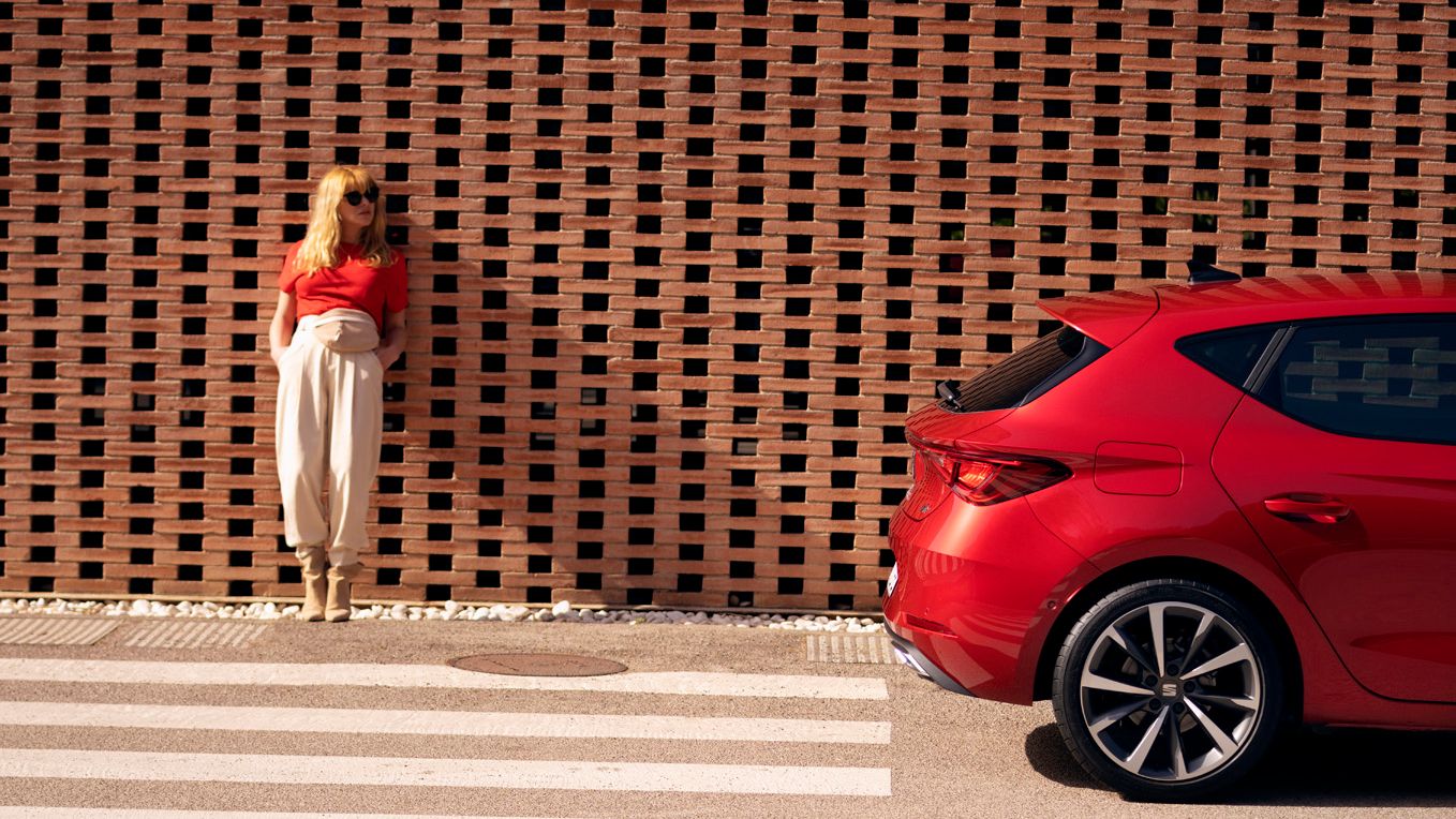Frau lehnt an einer Wand, daneben parkt ein roter SEAT Leon