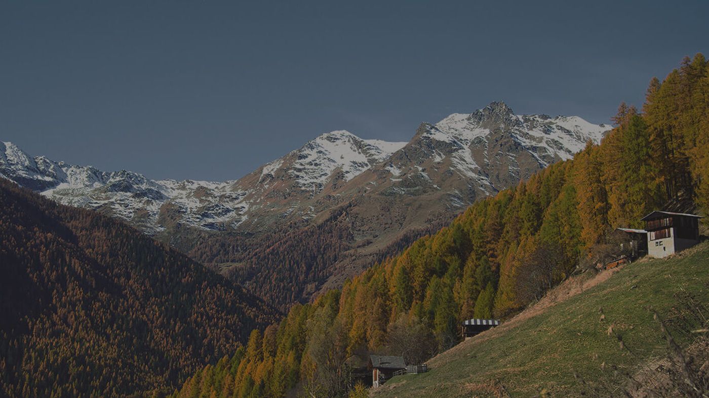 Zu sehen ist eine Berglandschaft, auf der Wiese davor stehen zwei kleine Hütten 