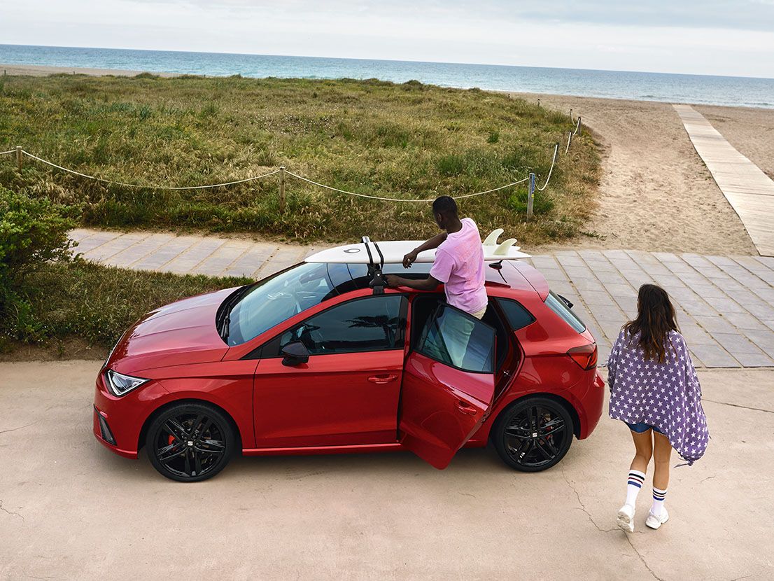 Ein Mann befestigt ein Surfbrett auf dem Dachträger eines SEAT Ibiza