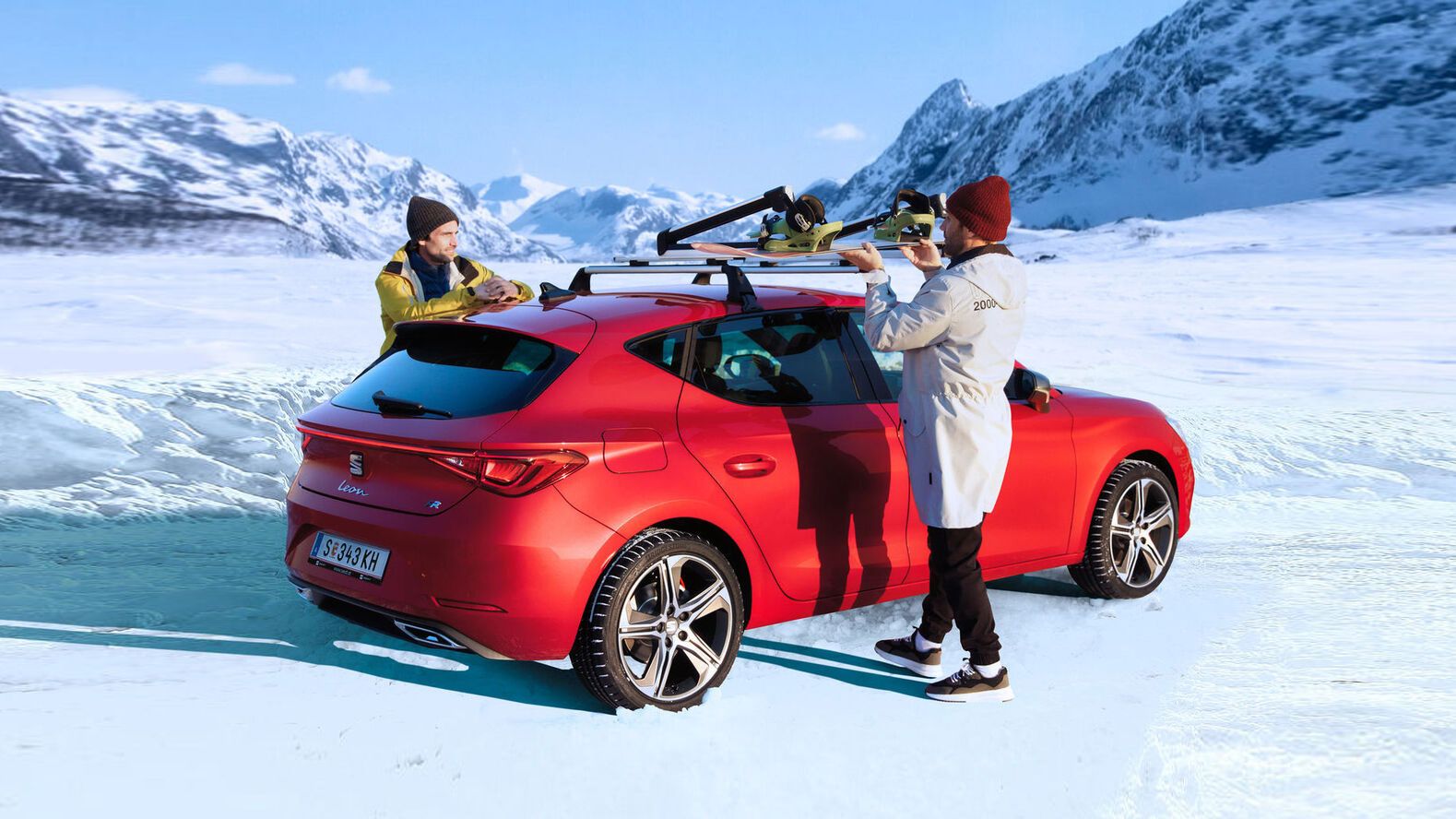 Ein roter SEAT Leon steht auf einer verschneiten Fahrbahn, während zwei Personen gerade Dachträger am Fahrzeug montieren